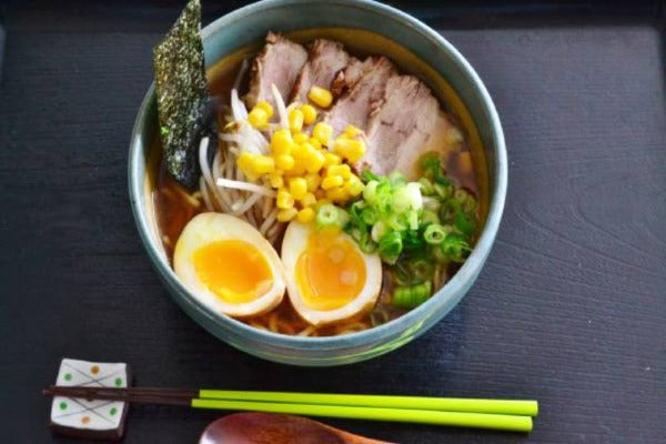 A shoyu ramen on a black tray with chopsticks.
